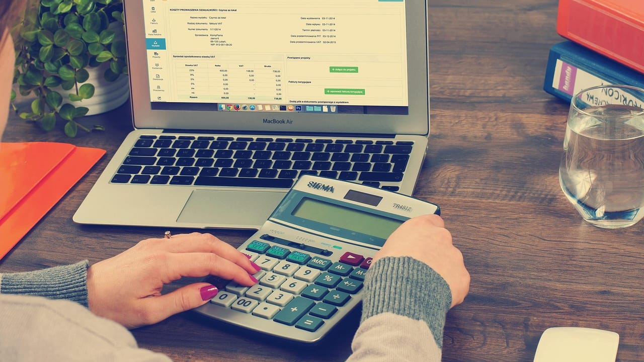 An accountant working through figures on a calculator beside a laptop